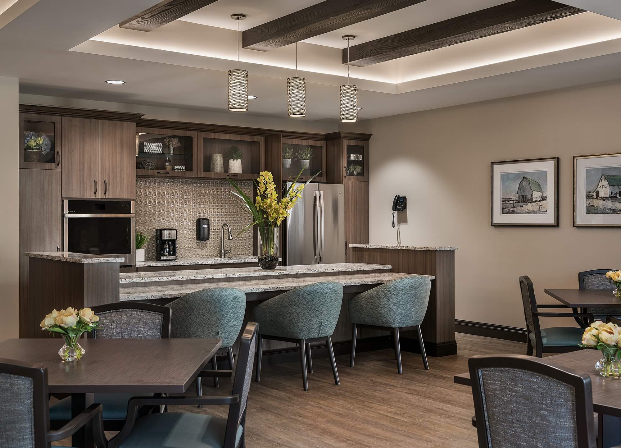 Elegant community kitchen with sleek appliances, pendant lights, and a large vase with yellow flowers.