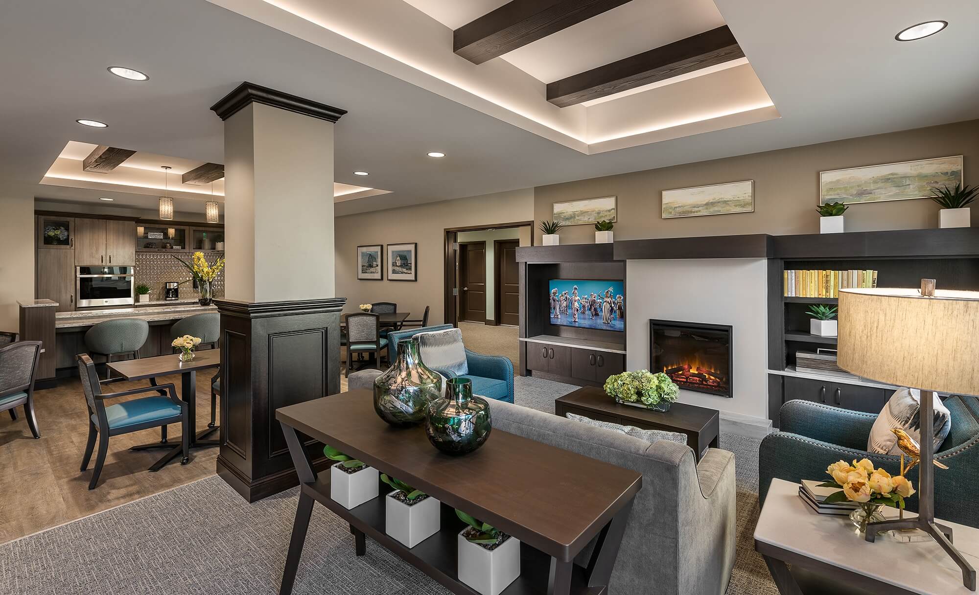 Elegant living space with a seating area around a fireplace and entertainment center, near a kitchen.